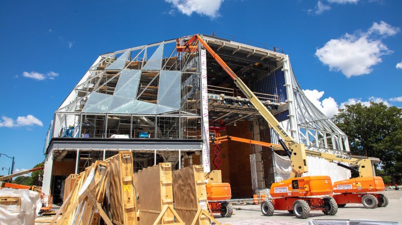 Construction on a large glass building with a crane in front of it 