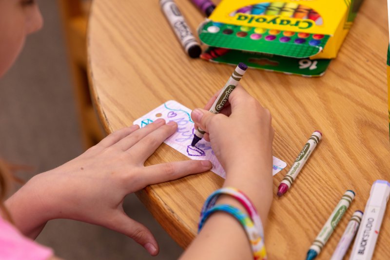 A young girl drawing with crayons on a small slip of paper