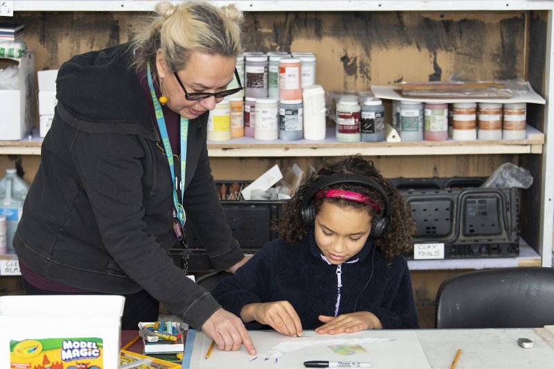 A woman instructs a young girl on an artmaking activity