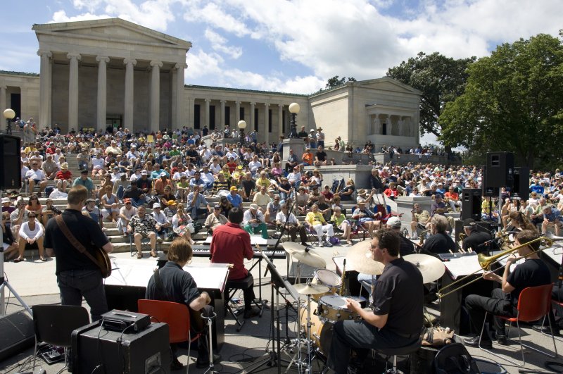 A large crowd sits around the outside of a museum to watch a jazz band perform