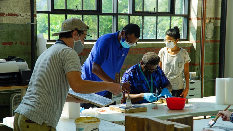 Three men and one woman wearing masks work on an art project