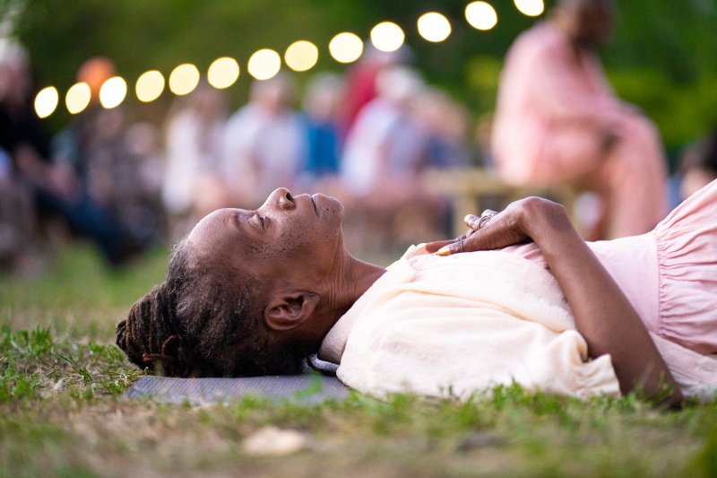 An African American woman laying in the grass with her hands resting on her chest 