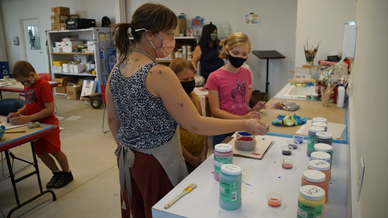 A woman helping two young girls with a clay art project