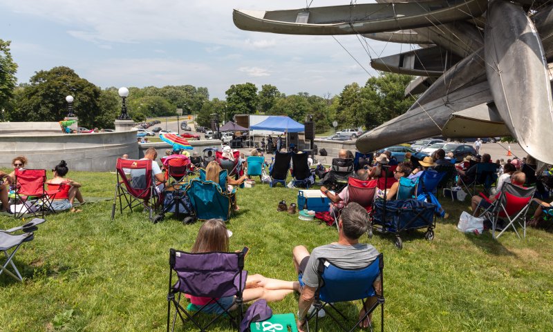 People sitting in lawn chairs listening to a jazz performance outdoors