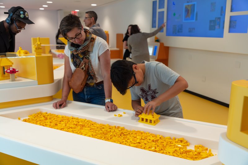 A mother and son building with yellow legos in a white room with yellow floors (a creative space in a museum)