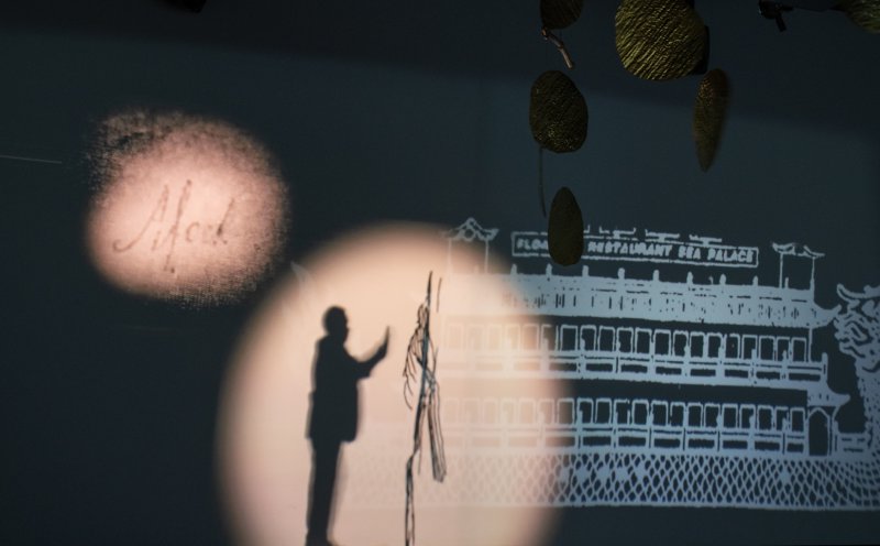 An installation video showing the silhouette of a man in a circle of light with an illustrated ship behind him 