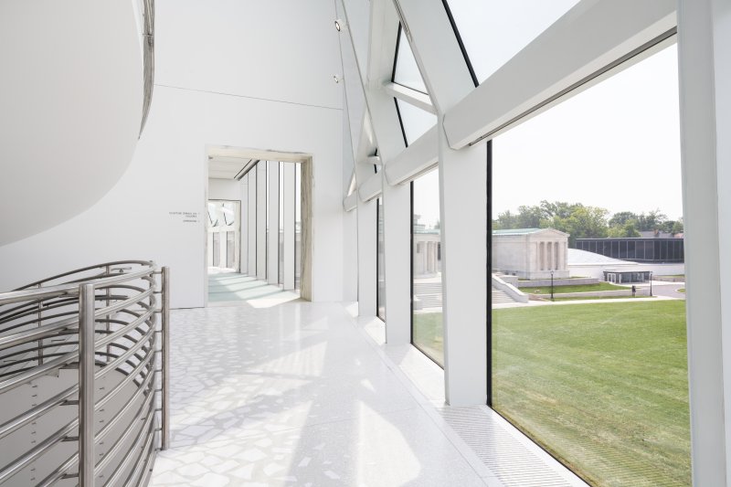 A white indoor terrace with a curved wall/window overlooking a museum campus