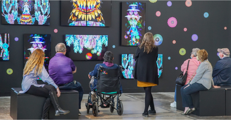 A group of people on a tour in an art gallery with a wall that has digital screens