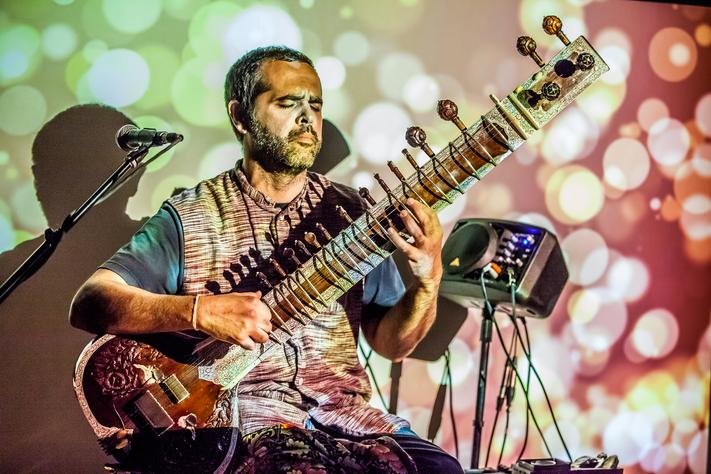 A man playing a sitar with bright red and green lights shining on him