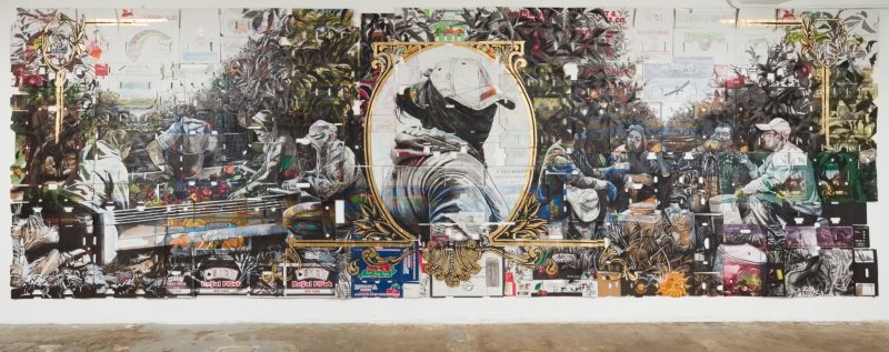 A large artwork takes up most of a wall, mimicking the look of a dollar bill but with imagery calling to agricultural labor in black ink and subdued colors, made on cardboard boxes