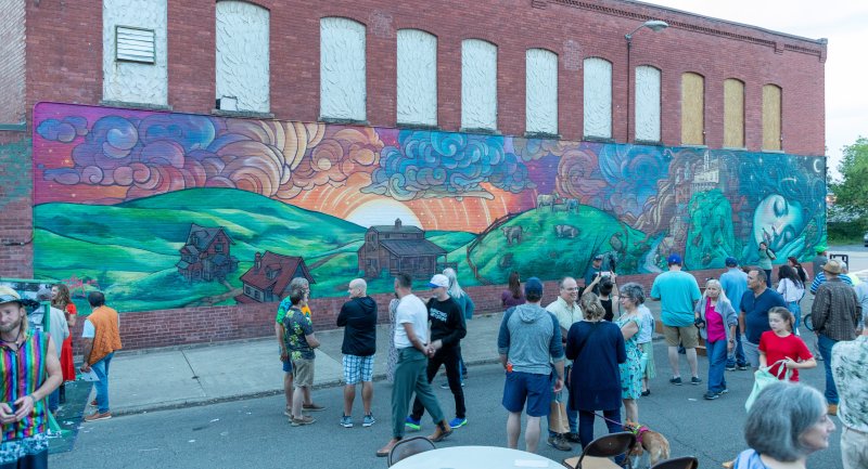 a mural of a sleeping green giantess on a brick building with a crowd of people surrounding it