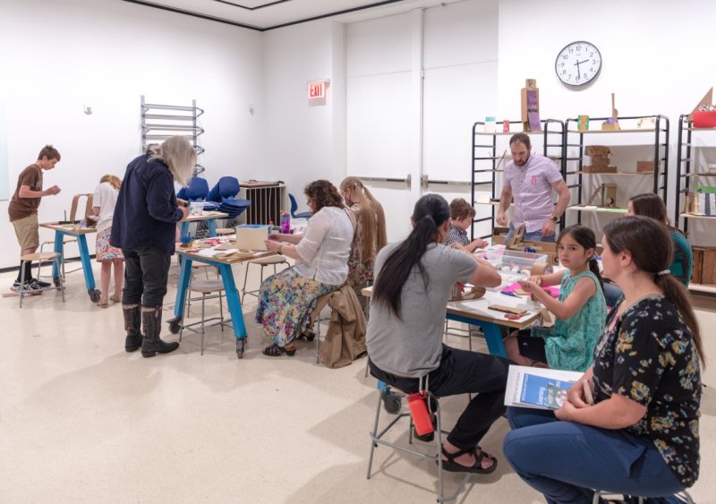A large art class filled with adults and children working on projects