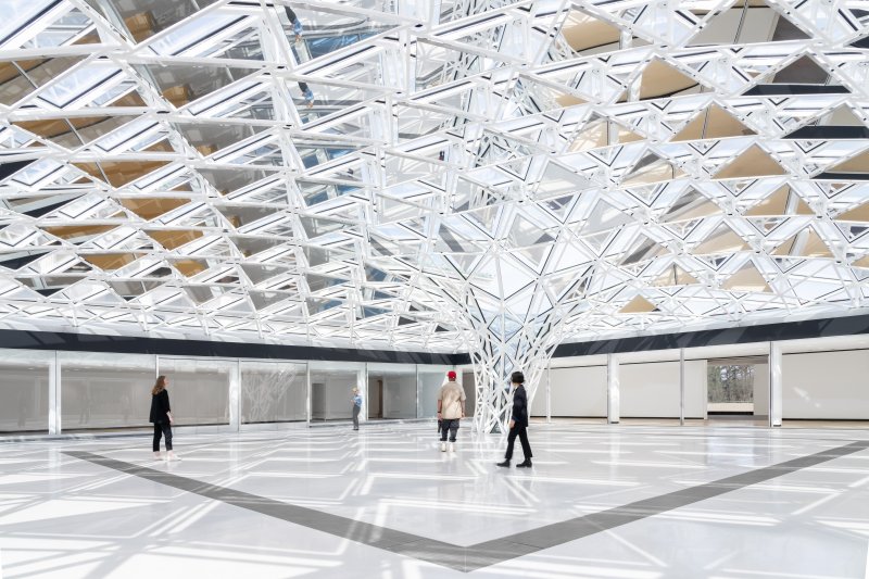 A glas tiled canopy ceiling that funnels down to a white floor. Three people are walking around the open white space