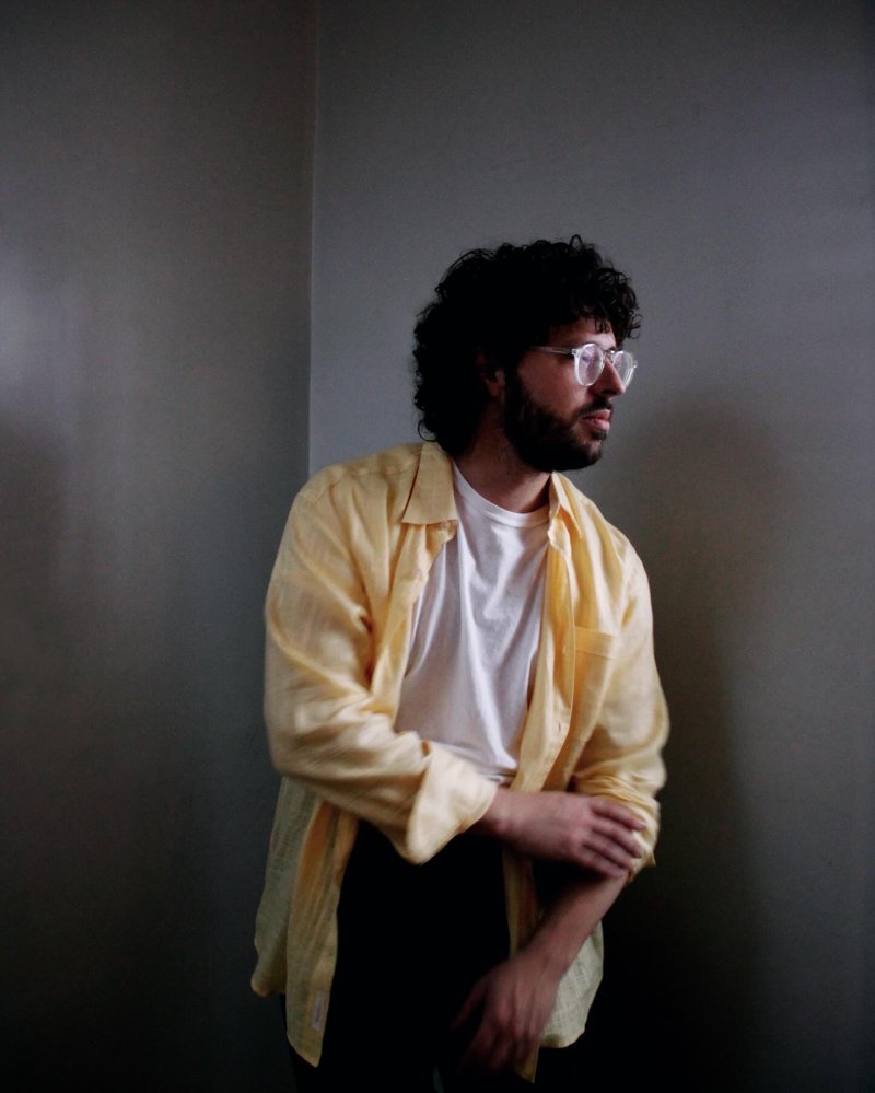 a man wearing a yellow button down with curly hair and glasses looking away from the camera