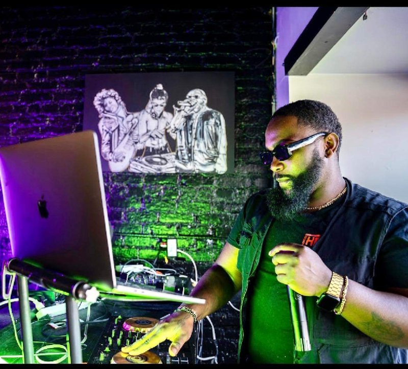 A DJ with his equipment surrounded by purple and green lights