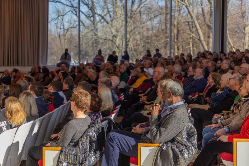 A crowd of people sitting in an auditorium with a large window behind them