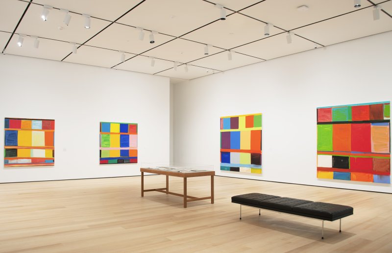 Gallery view of four large vibrant grid-like paintings 