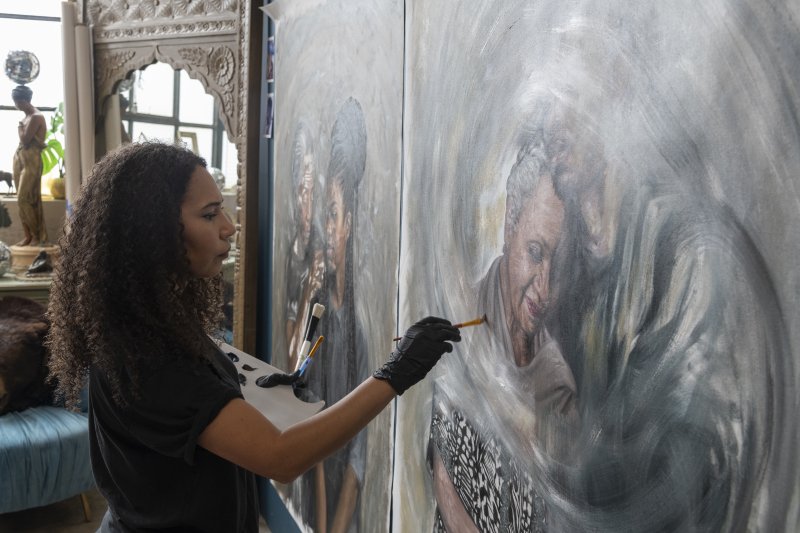 A woman with dark curly hair painting a portrait on a wall