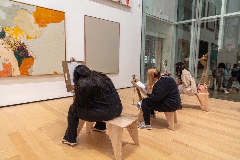 Three young women sitting on drawing horses sketching in an art gallery