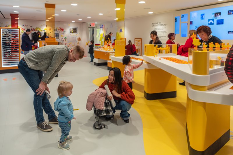 Families in a white and yellow themed play space with areas to build with legos