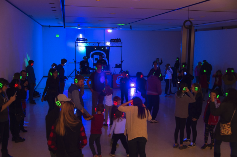 A dark room with a DJ and a crowd with light up headphones