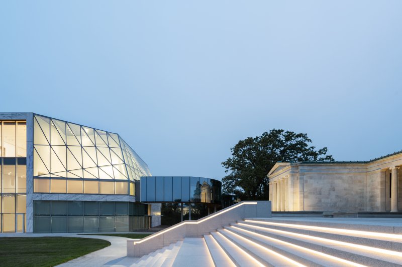 A glass museum building connected to a marble museum building by a glass bridge