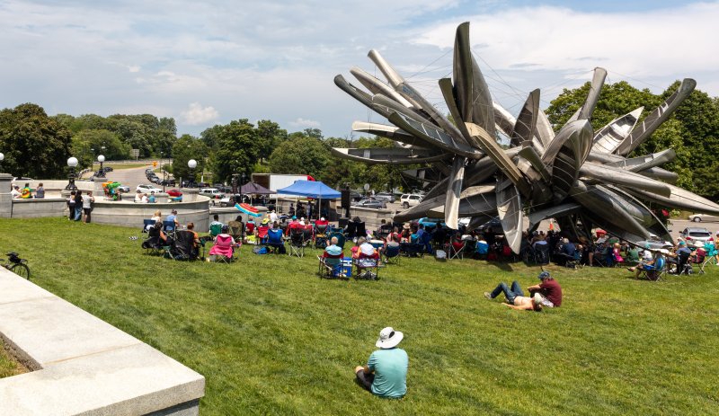 A crowd of people gathered outdoors near a large sculpture made of canoes