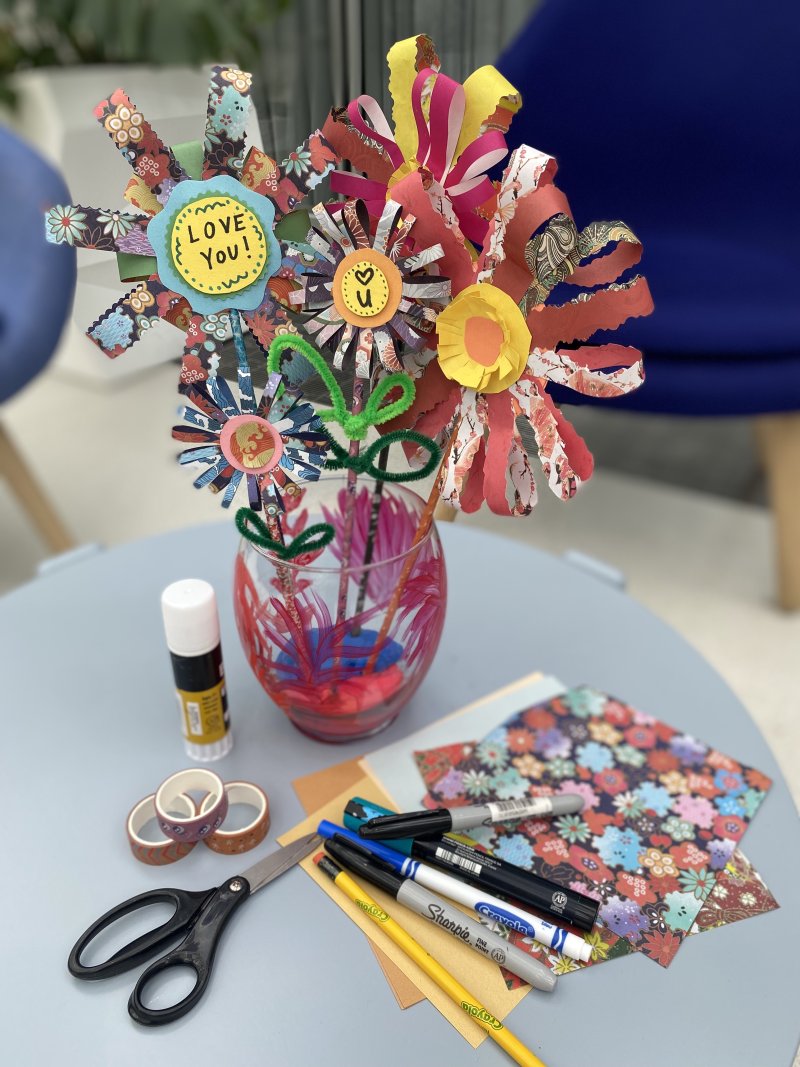 Paper flowers in a vase with art supplies around them