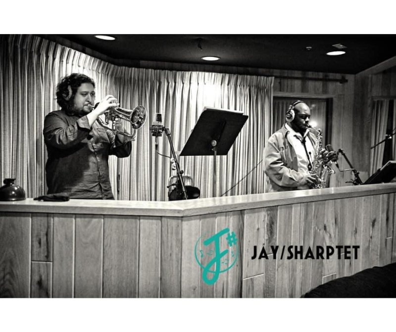 Black and white photo of a man playing the trumpet and another playing the saxophone 