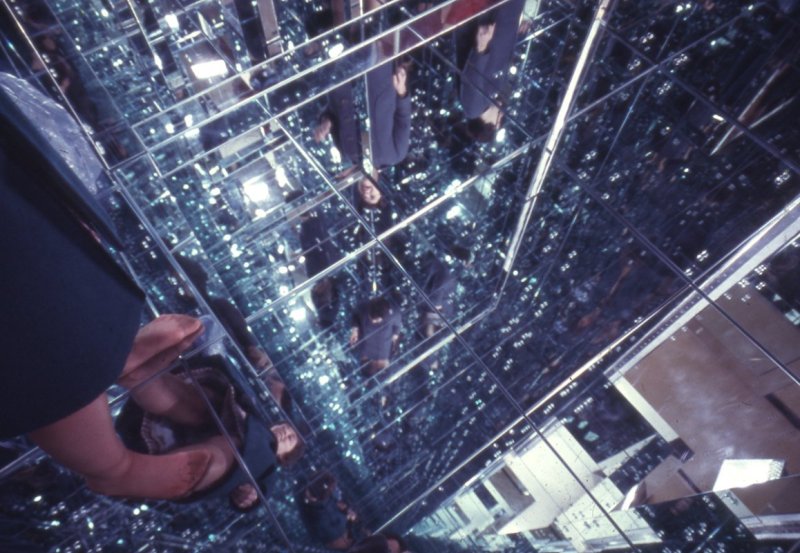 A film photo facing the ground of a room full of mirrors and two pairs of legs are visible