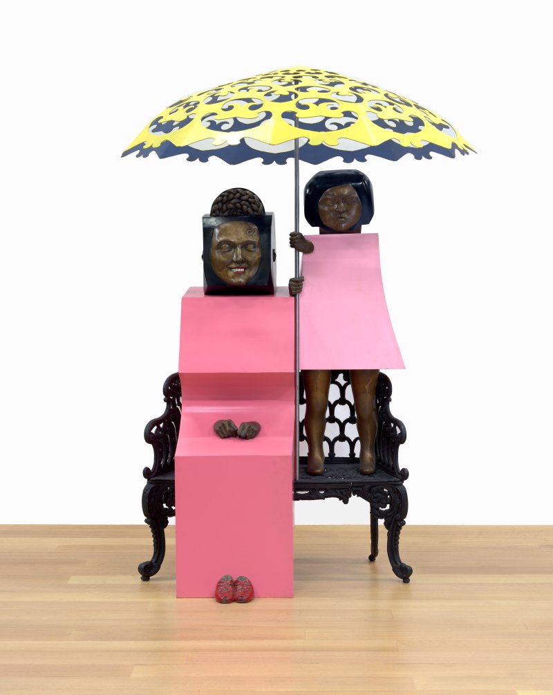 A Marisol sculpture of a woman and a young girl sitting on a bench with a parasol in between theml 