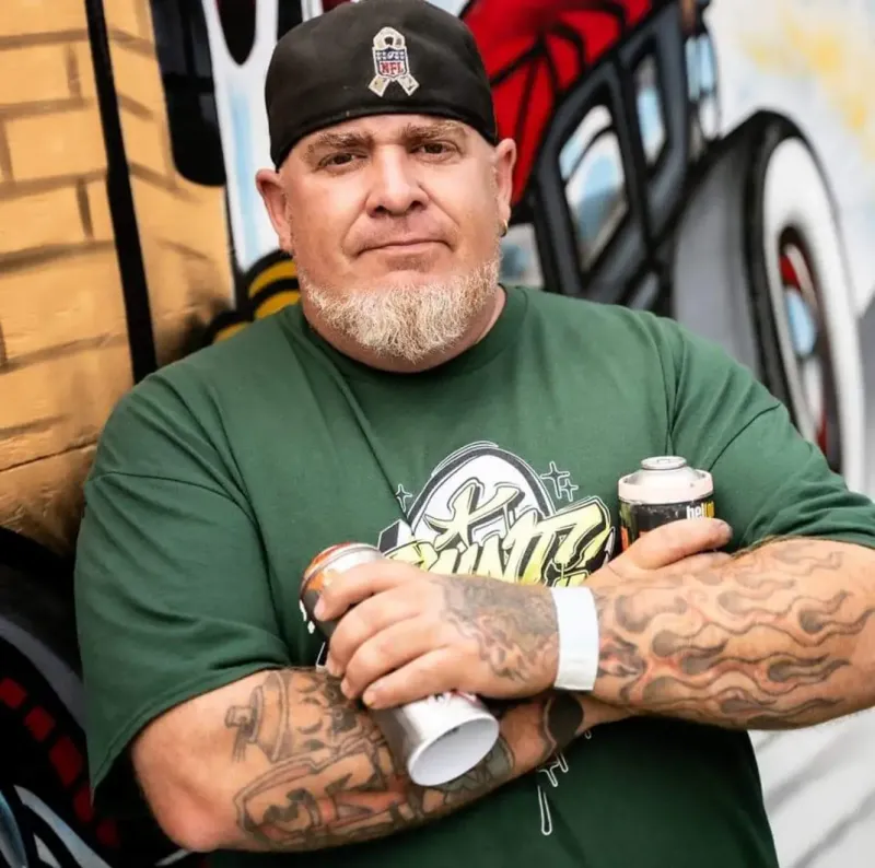 Headshot of a man wearing a green shirt holding a spray paint can