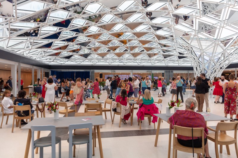 People sitting at tables and dancing under a glass mosaic ceiling that funnels into the ground
