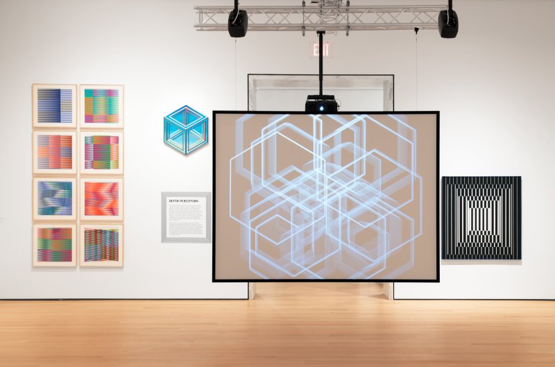 Installation view of an art gallery with a screen and artworks on white walls