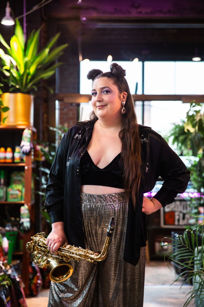 A person holding a saxophone with a backdrop filled with plants