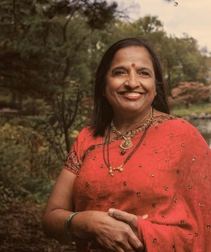 An Indian woman wearing a red sari in front of a woodland backdrop
