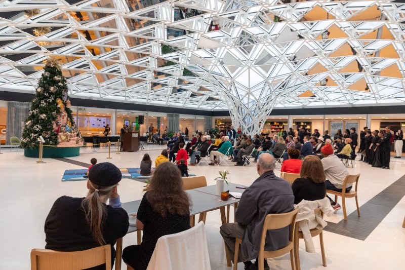 People gathered around a large Christmas tree under a glass mosaic ceiling