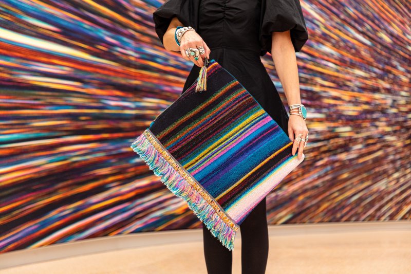 A person holding a vibrant handbag in front of a vibrant backdrop