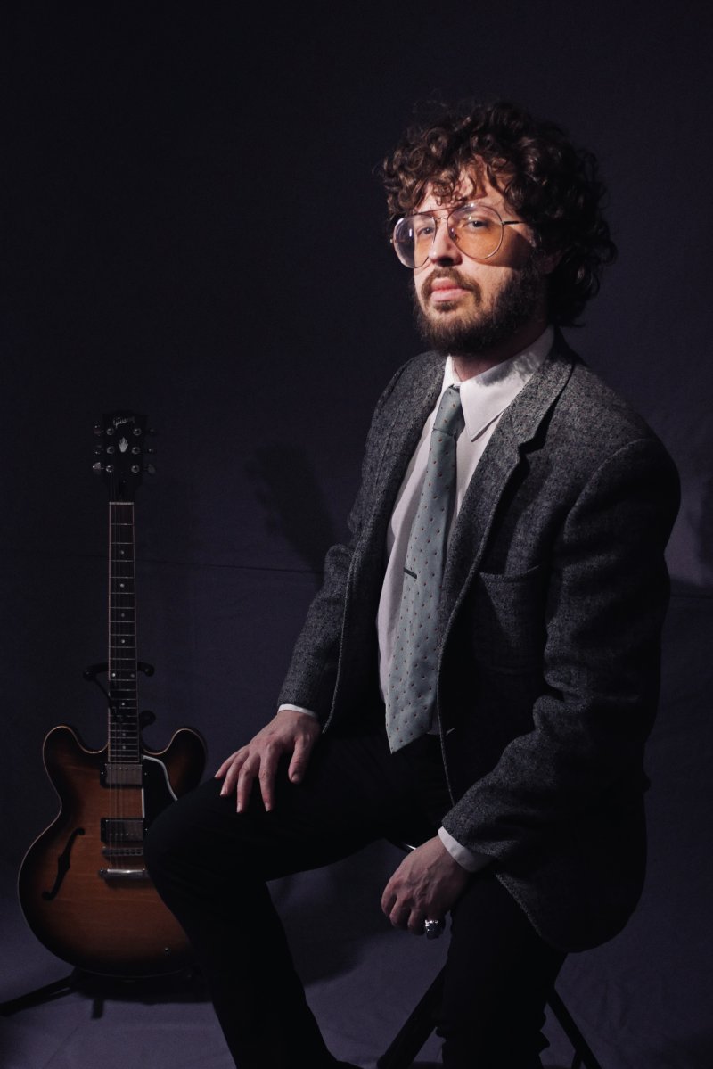 A person sitting next to a guitar on stand