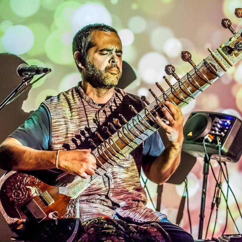 In vibrant lighting a person plays a sitar