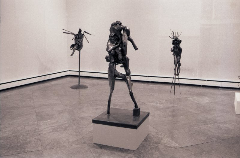 Black and white image of three metal abstract sculptures in a gallery space