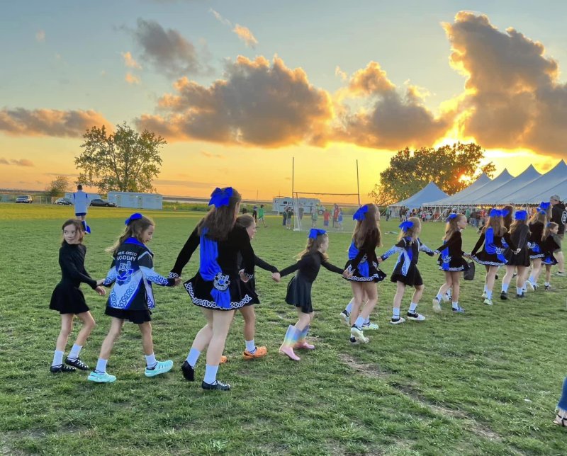 A group of young Irish dancers holding hands in a line outdoors