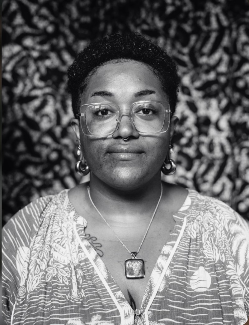 Black and white image of a person with short dark hair, wearing large framed glasses