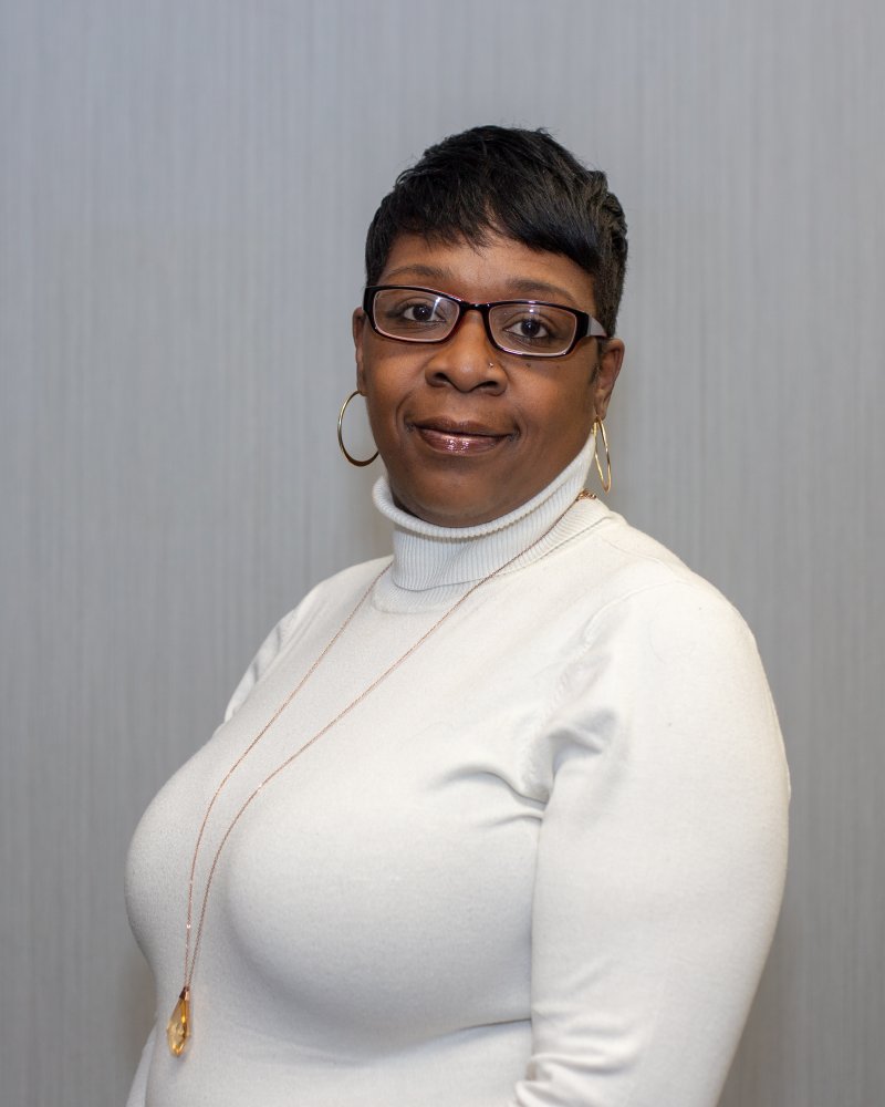 Headshot of a person with short dark hair and large framed glasses wearing a white turtleneck
