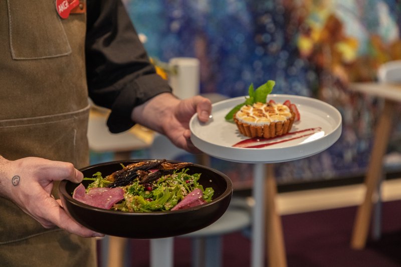 Hands holding two plates of food in a dining area