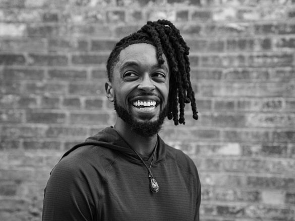 Black and white image of a person smiling in front of a brick wall