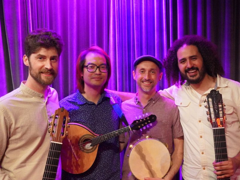 Four individuals holding instruments smiling in front of a purple curtain