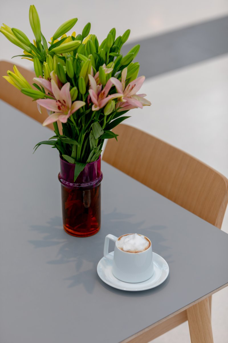 A bouquet of flowers in a vase with a cup of coffee next to it