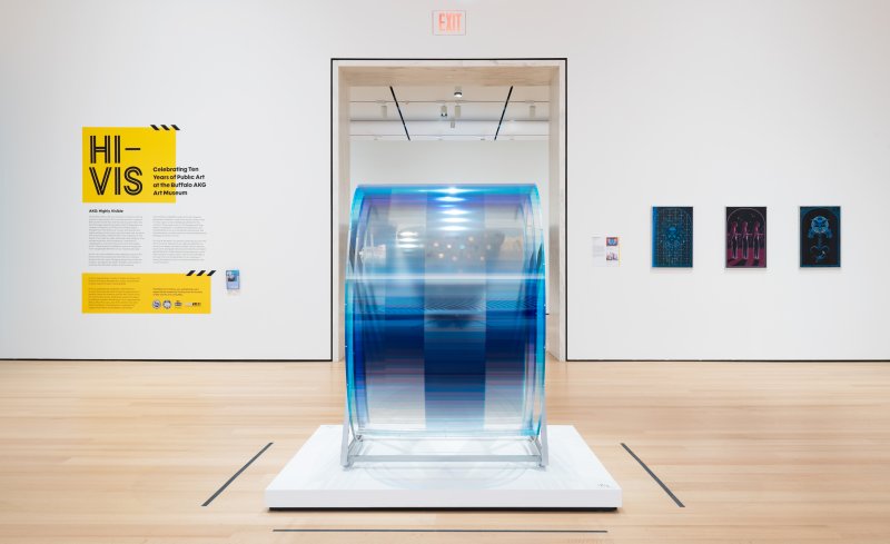 Installation view of a gallery with a spinning sculpture in the center and yellow wall vinyl that reads "Hi-Vis" 