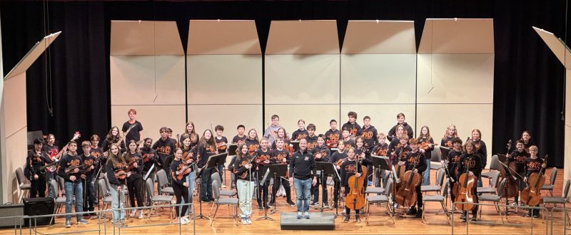 A middle school orchestra standing on a stage